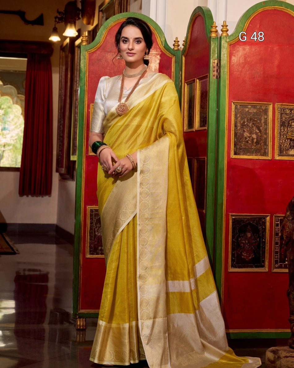 Woman in a yellow saree standing in a decorated room with red walls and gold accents.