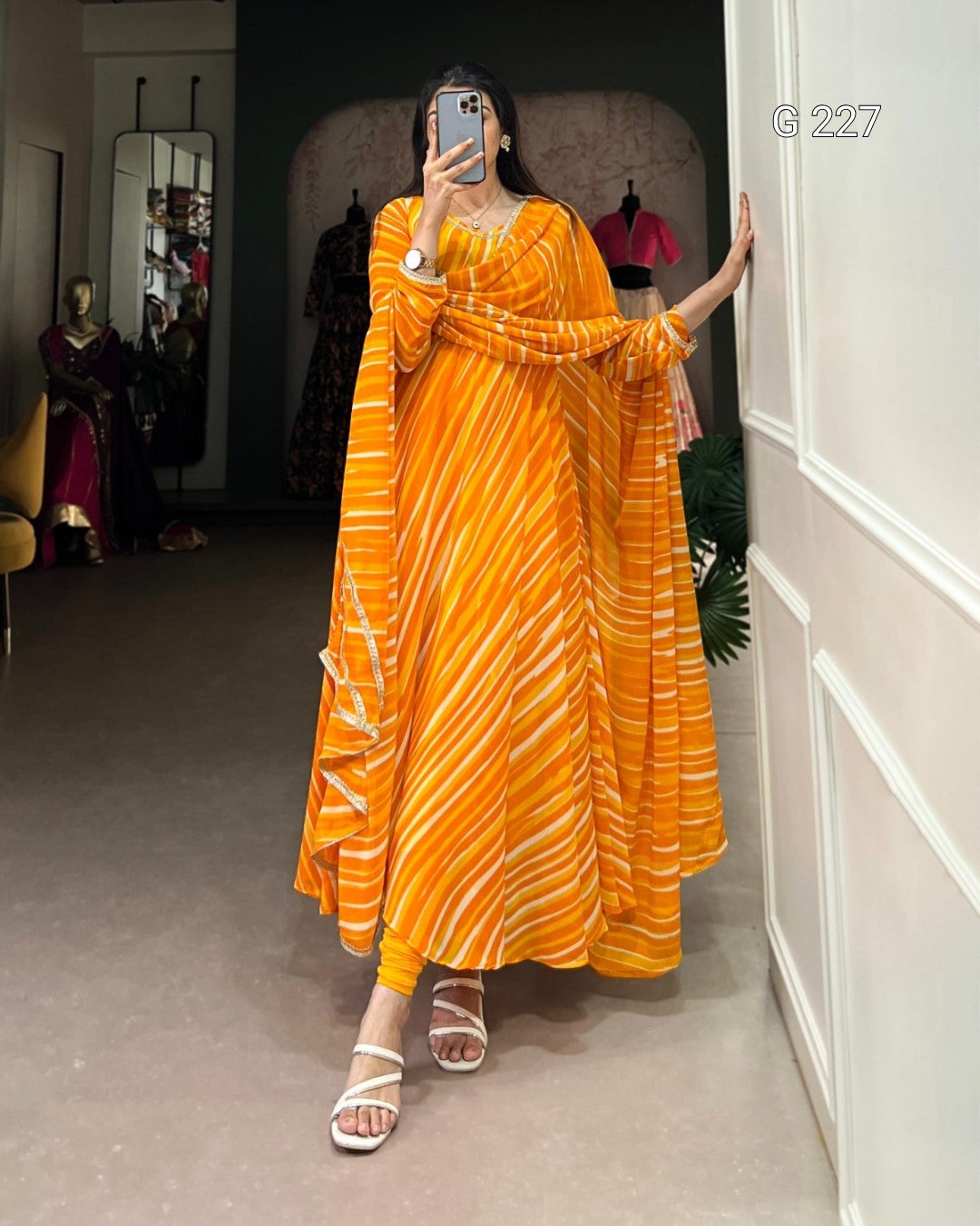 Person wearing an orange dress taking a mirror selfie in a room.