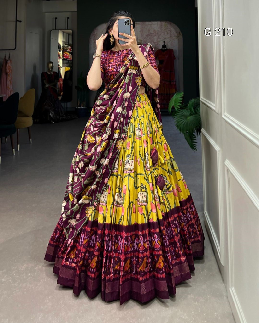 Person wearing a colorful traditional outfit with a patterned dress and dupatta in a room.