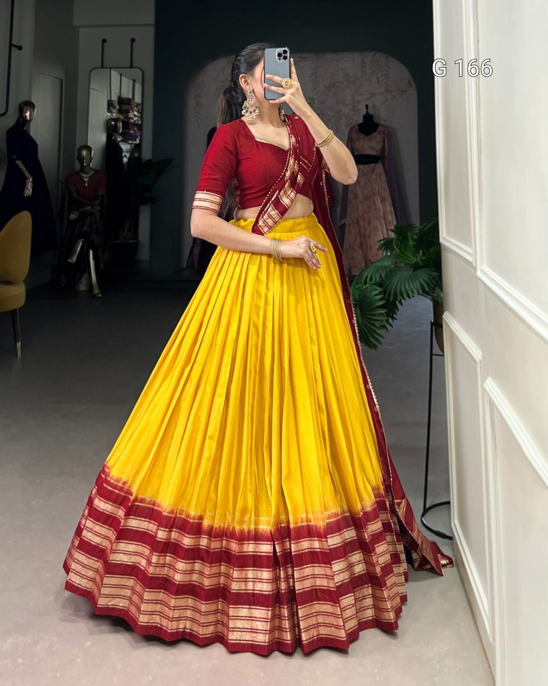 Woman wearing a red blouse and yellow saree with a striped border, standing in a room.