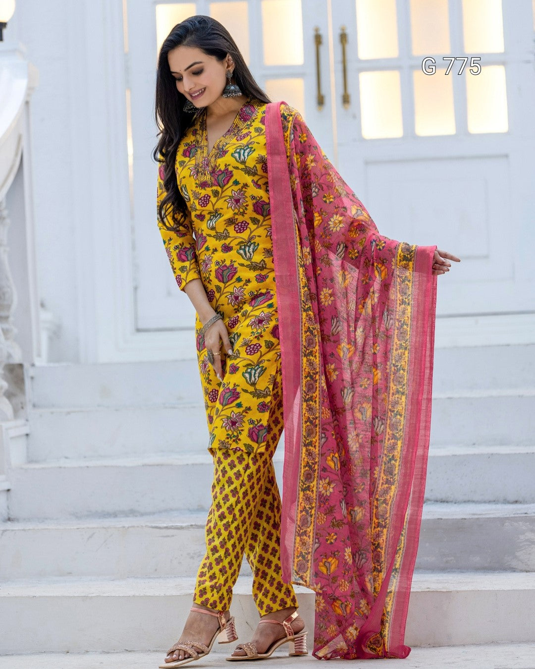 Woman wearing a yellow and pink traditional outfit with a floral pattern on a white staircase background.