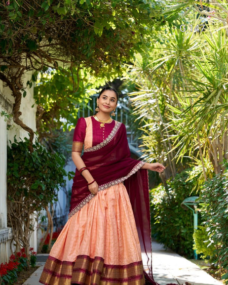 Woman in a traditional maroon and peach saree standing in a garden.