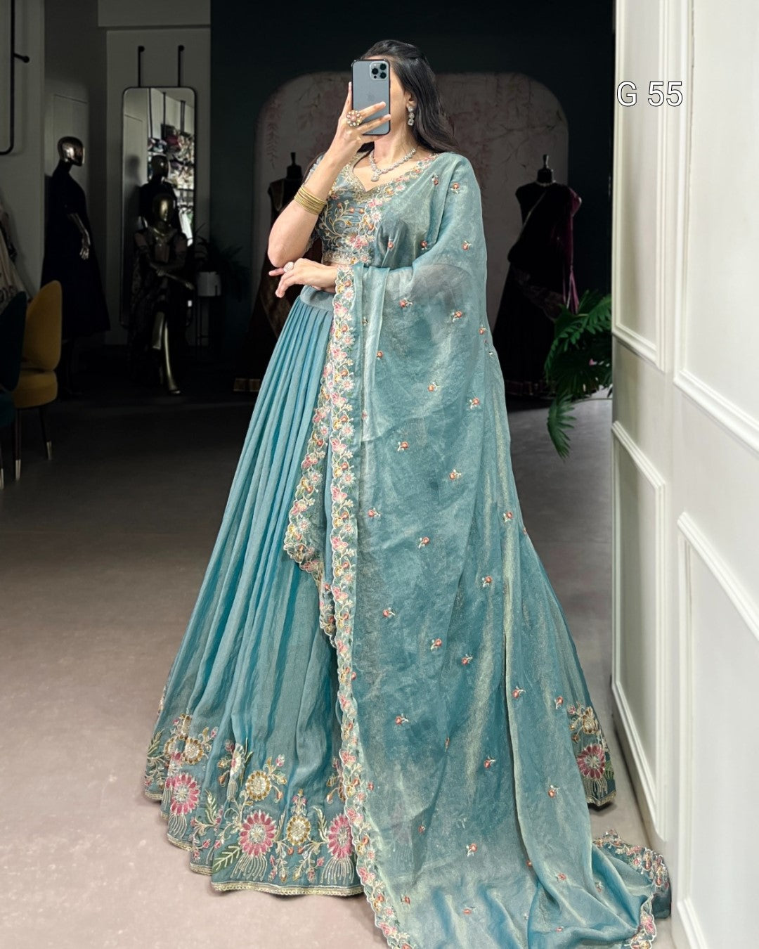 Person wearing a light blue saree with floral embroidery in a room.