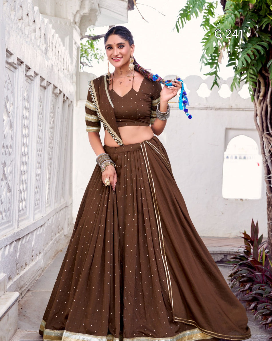 Woman in a brown traditional outfit with gold details standing in a decorative indoor setting.