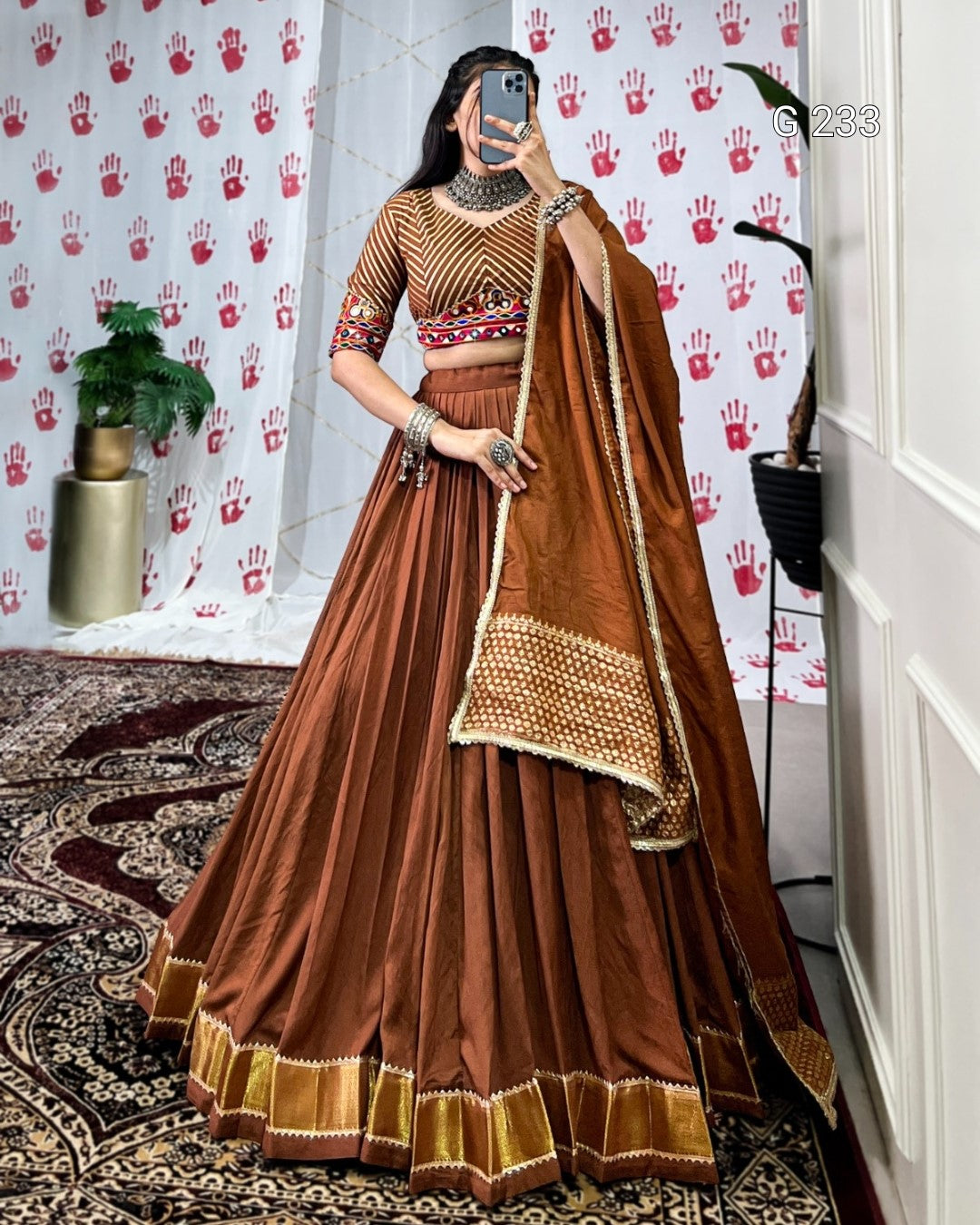 Woman in a traditional brown and gold outfit standing in a room with decorative wallpaper.