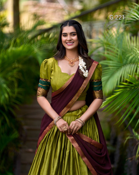 Woman in a green and maroon saree standing in a natural setting with greenery.