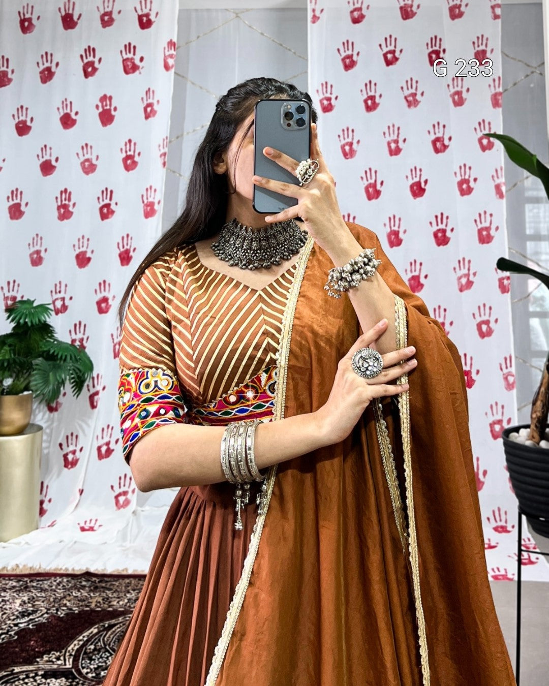 Person wearing a traditional outfit with jewelry in front of a patterned curtain