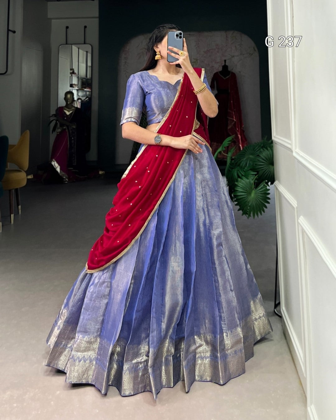 Woman wearing a blue saree with a red blouse, standing in a room.