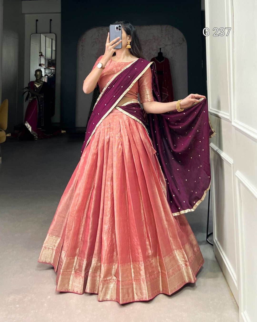 Person wearing a pink saree with a purple blouse, standing in a room.