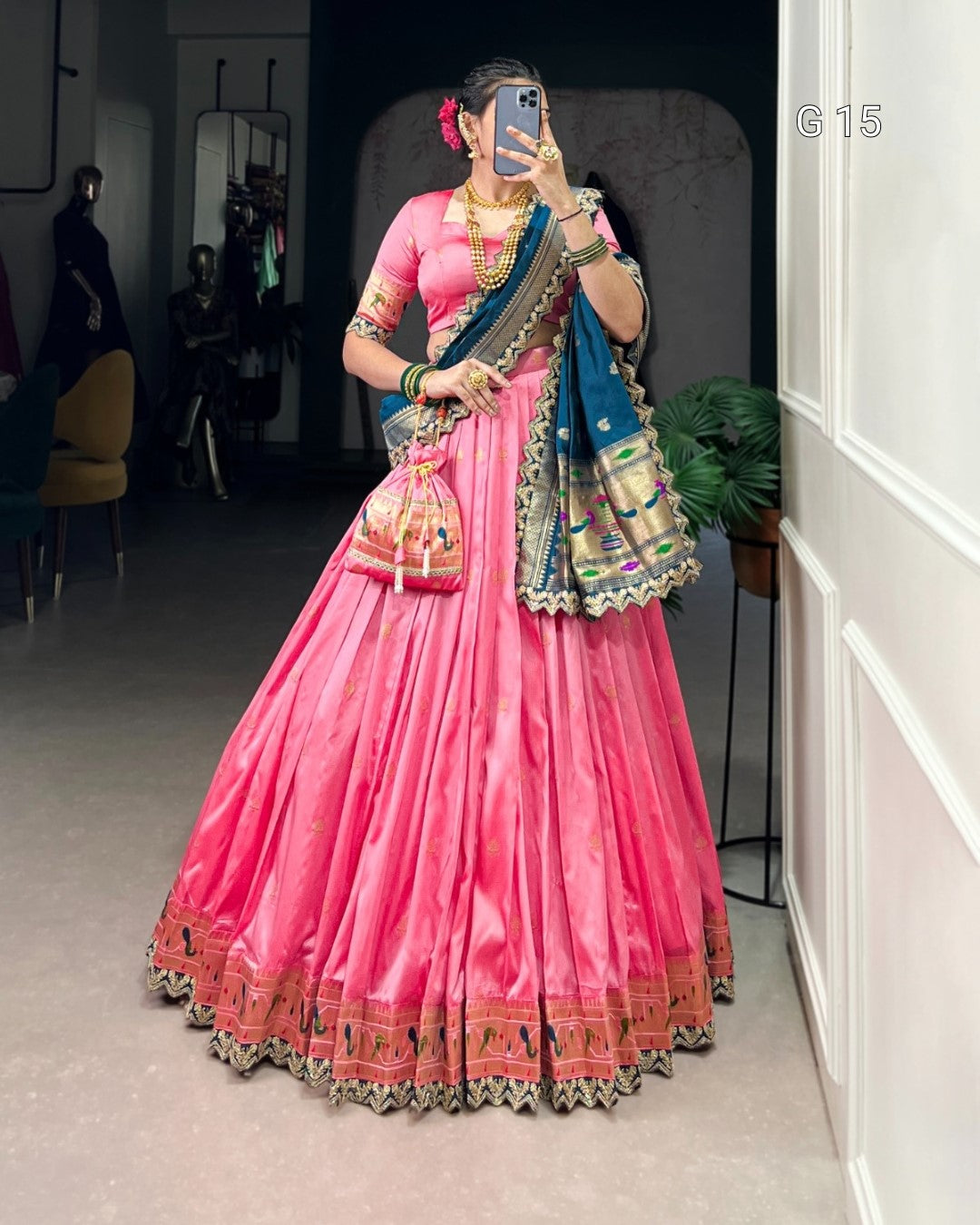 Person wearing a traditional pink saree with a blue blouse, holding a phone, in an indoor setting.