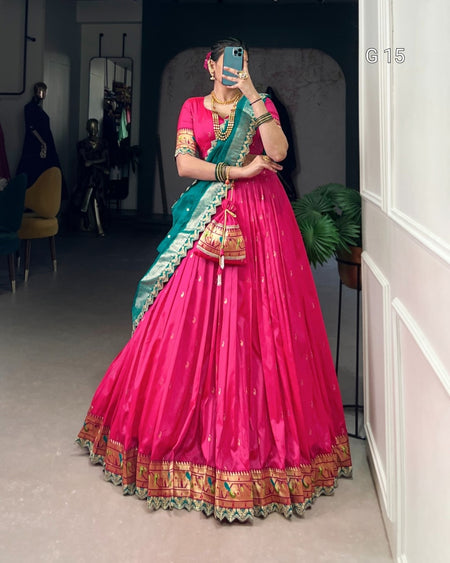 Person wearing a vibrant pink and green traditional outfit with intricate patterns, standing indoors.