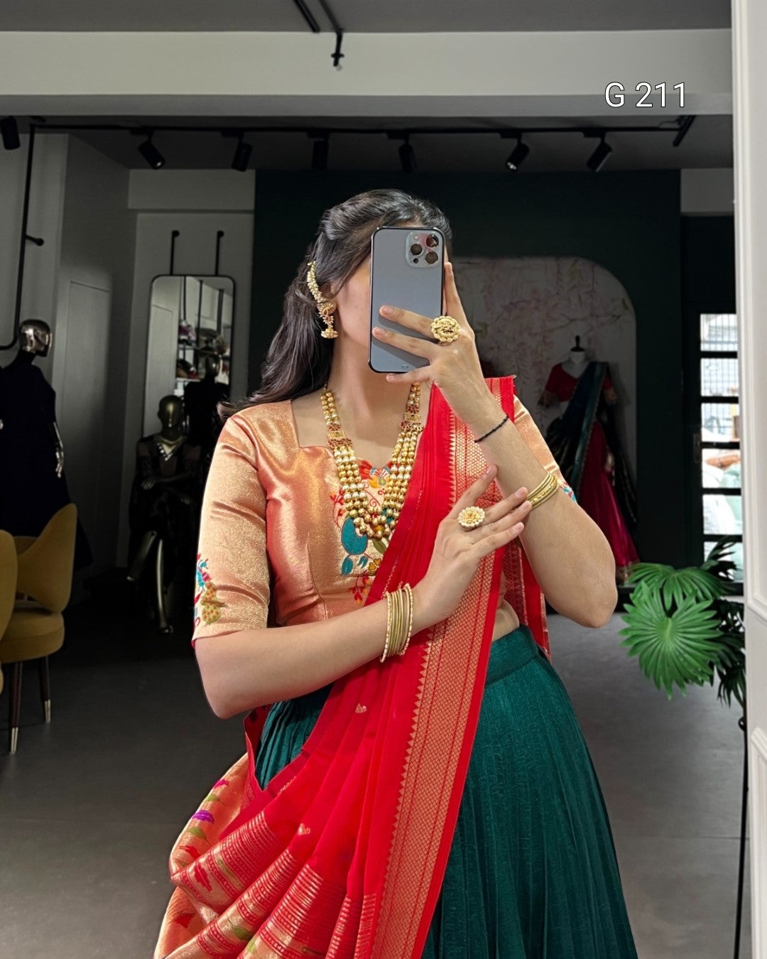 Woman in traditional outfit with jewelry taking a mirror selfie in a room.