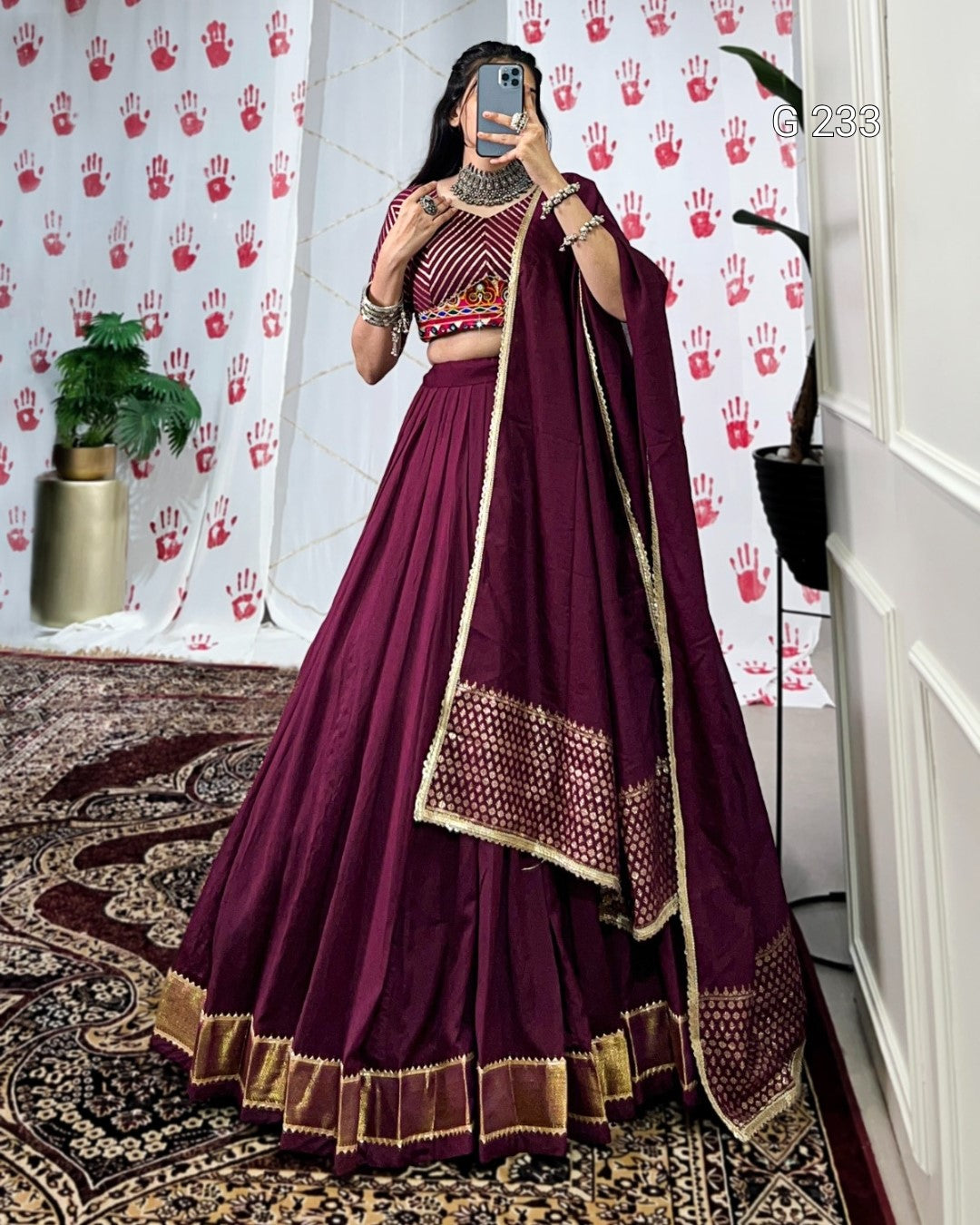 Person wearing a maroon traditional outfit with gold details in a room with patterned wallpaper.