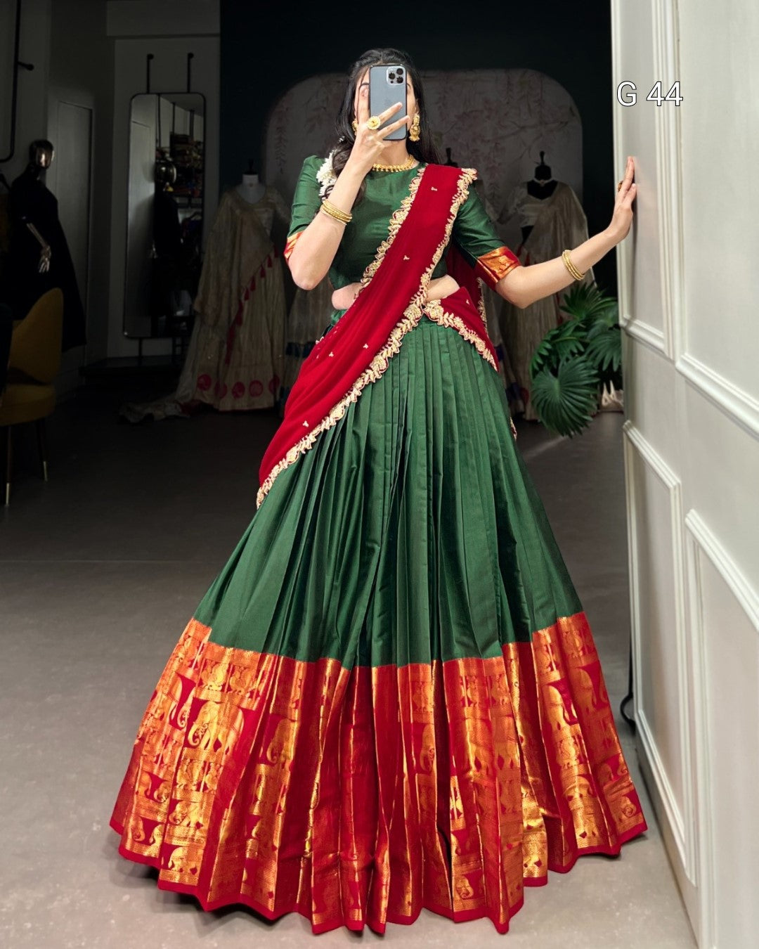 Person wearing a green and red traditional outfit with a saree, standing in a room.