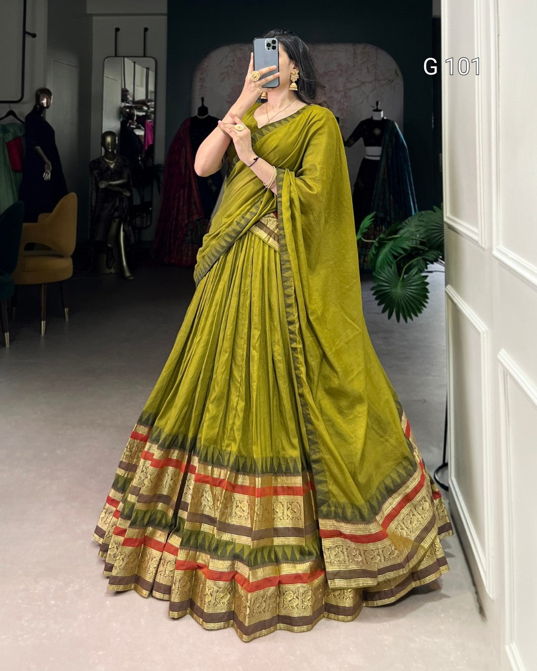 Woman wearing a green saree with red and gold border in a room.