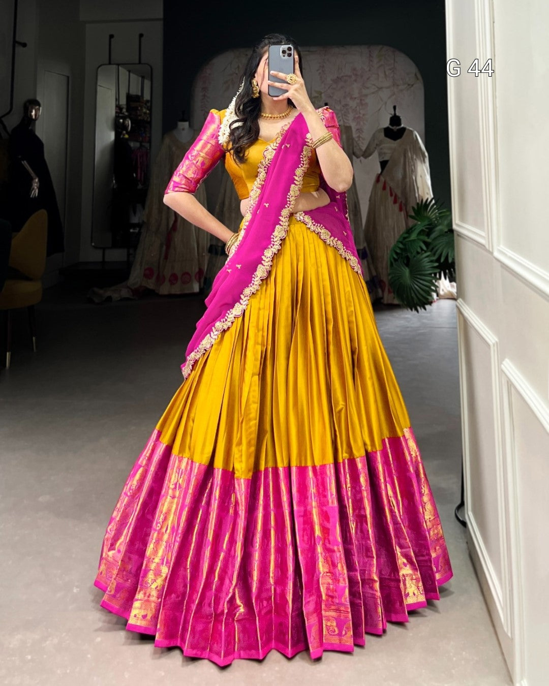Woman wearing a yellow and pink traditional outfit taking a mirror selfie.