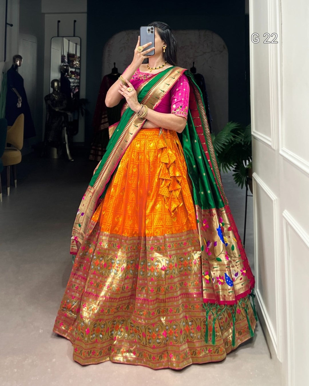 Woman in a traditional orange and green saree taking a mirror selfie.
