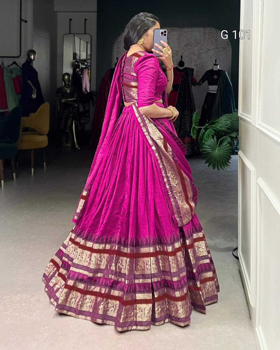 Woman in a vibrant pink saree with gold patterns taking a mirror selfie.