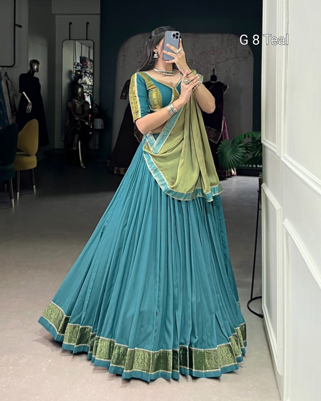 Woman wearing a blue and green saree taking a mirror selfie.