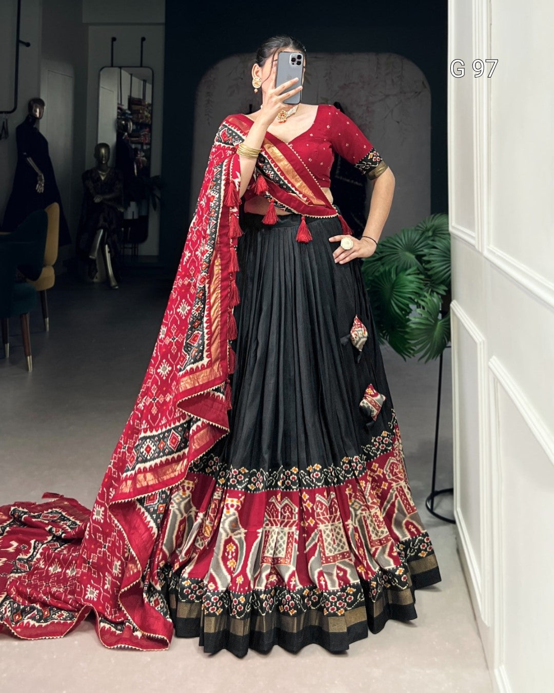 Woman wearing a traditional red and black saree with a patterned shawl, standing in a room.