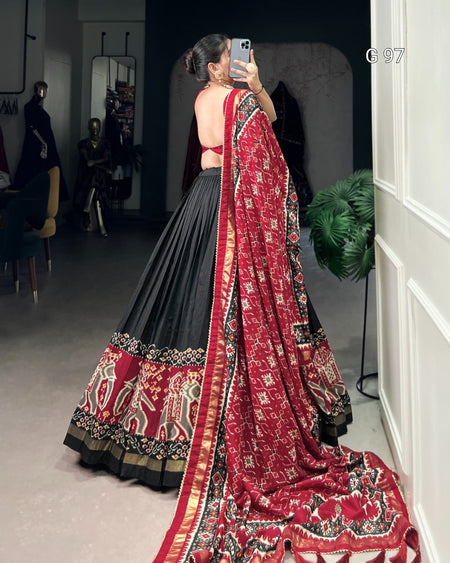 Person wearing a red and black traditional outfit with a long scarf in a room.