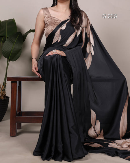 Woman wearing a black and beige saree with a plant and stool in the background