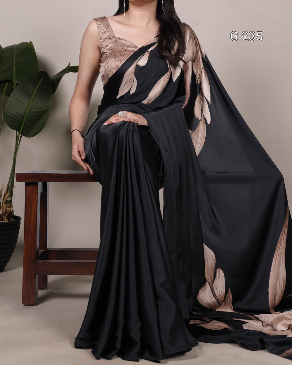 Woman wearing a black and beige saree with a plant and stool in the background