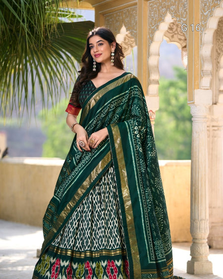 Woman wearing a green saree with a traditional design, standing in front of an architectural structure.