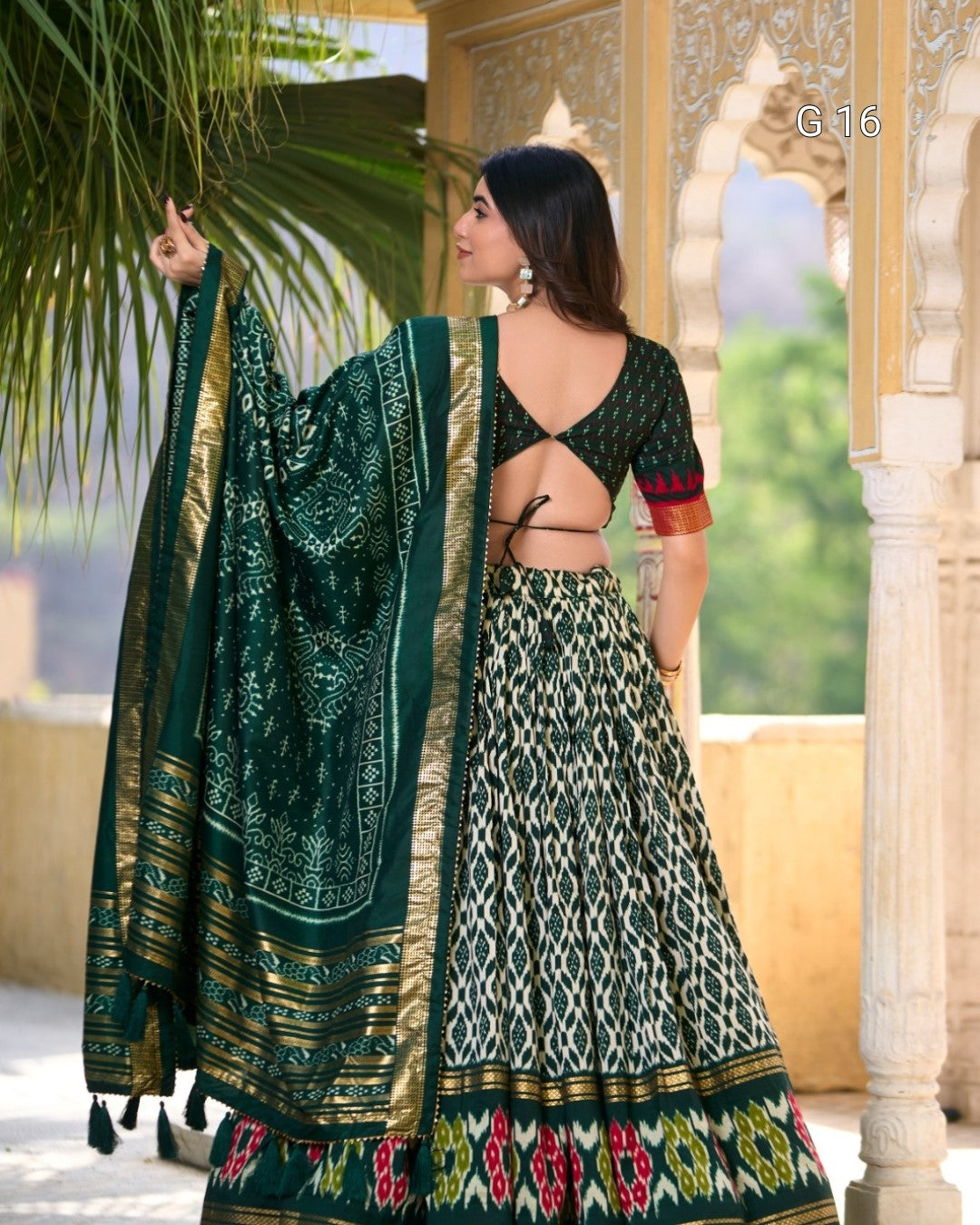 Woman in a traditional green and gold saree with a patterned design, standing outdoors.