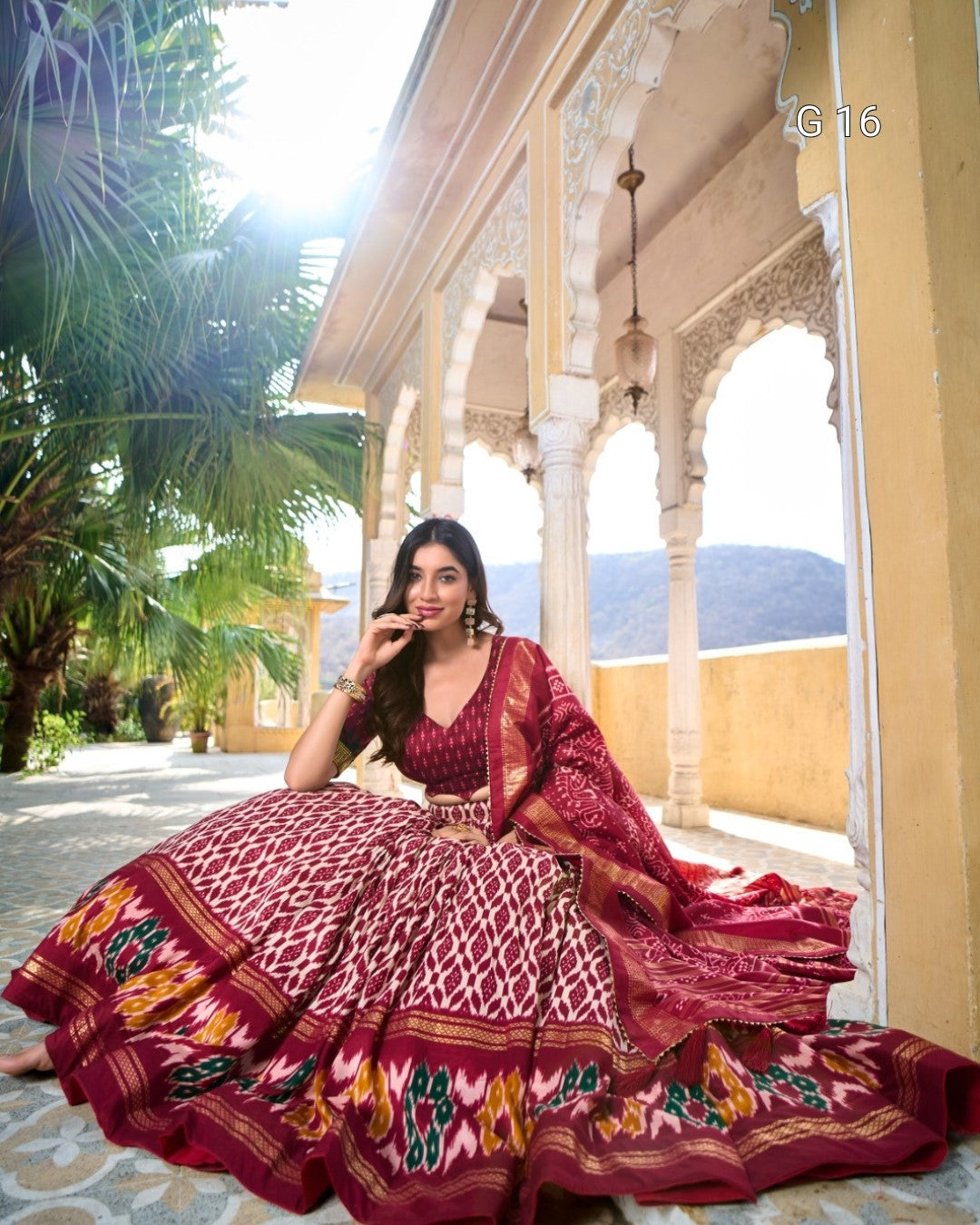 Woman in a traditional maroon and gold saree sitting on a porch with scenic background