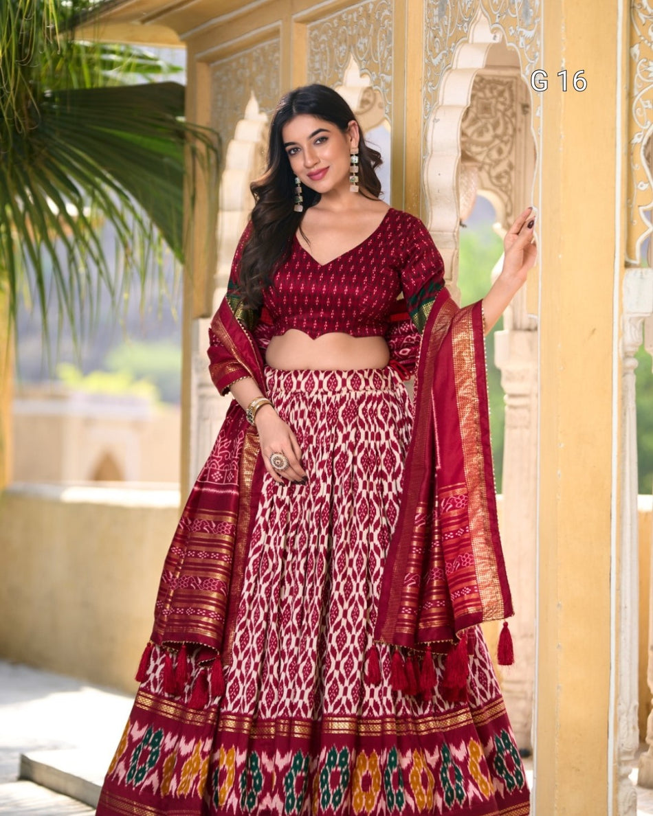 Woman in traditional maroon and white saree with intricate patterns, standing in a decorative setting.