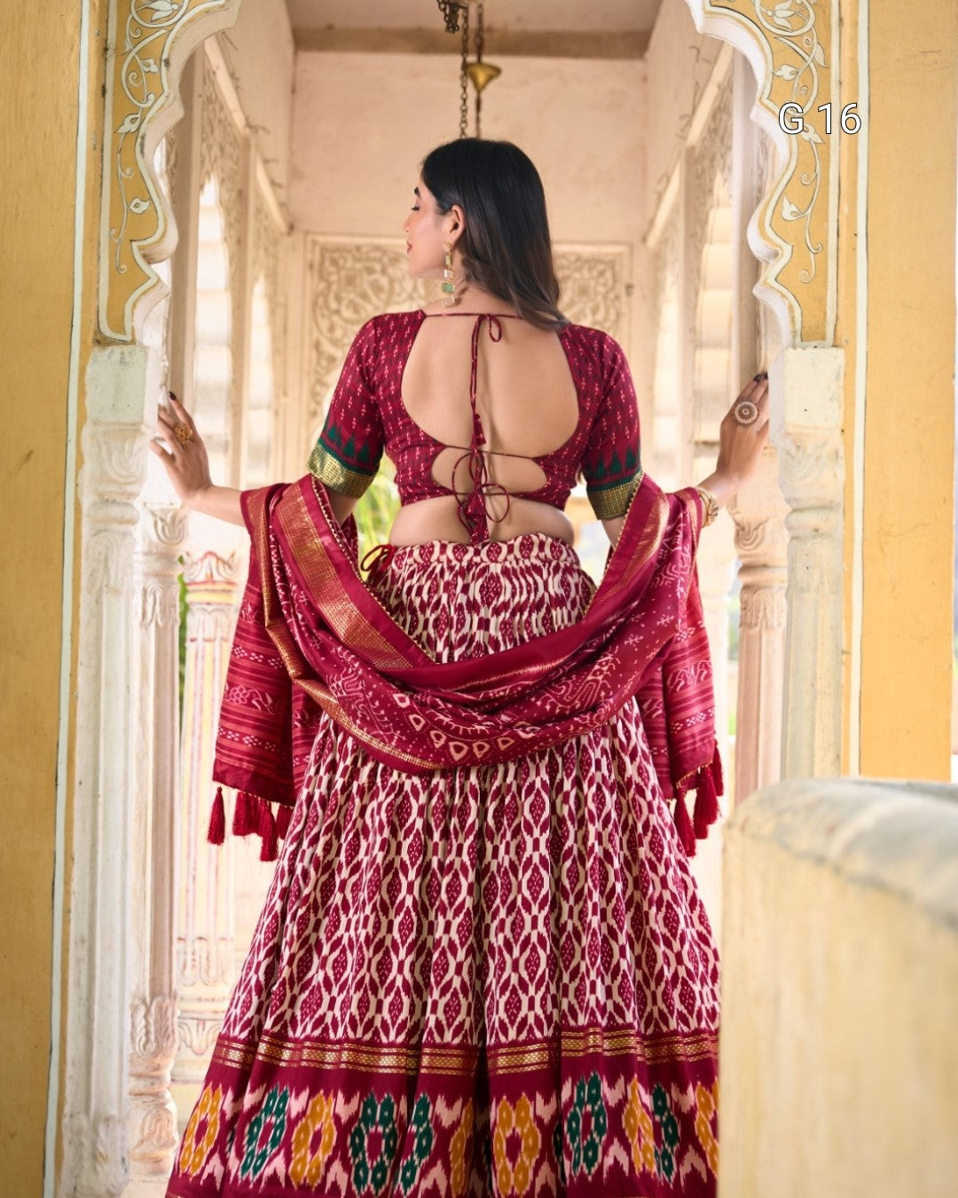 Woman in a traditional red and patterned outfit standing in an ornate doorway.