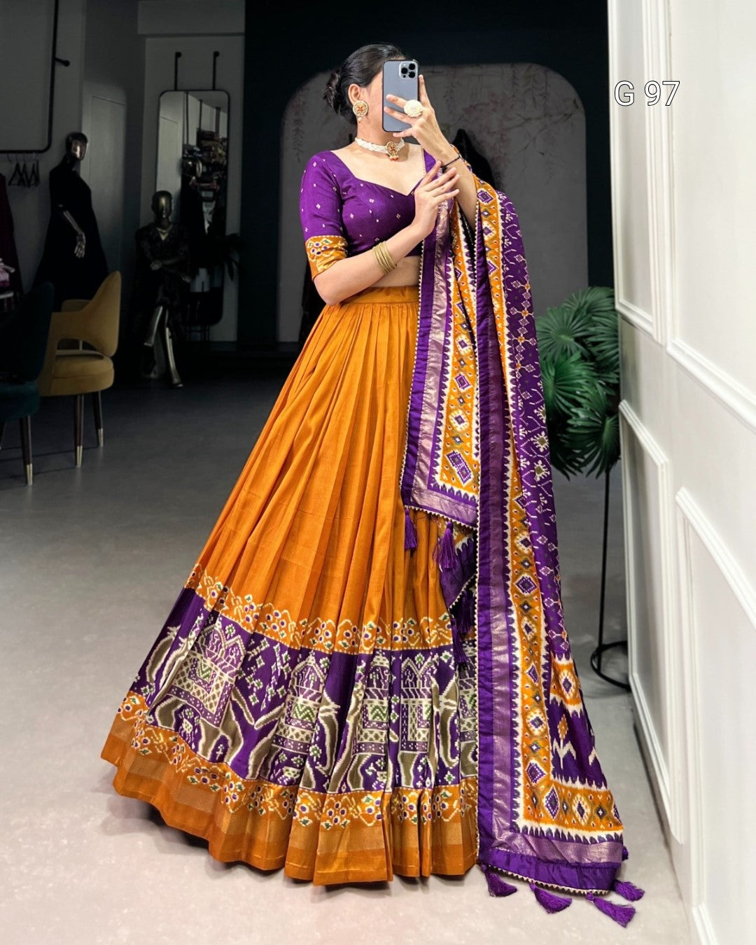 Woman wearing a traditional orange and purple outfit with a matching dupatta indoors.
