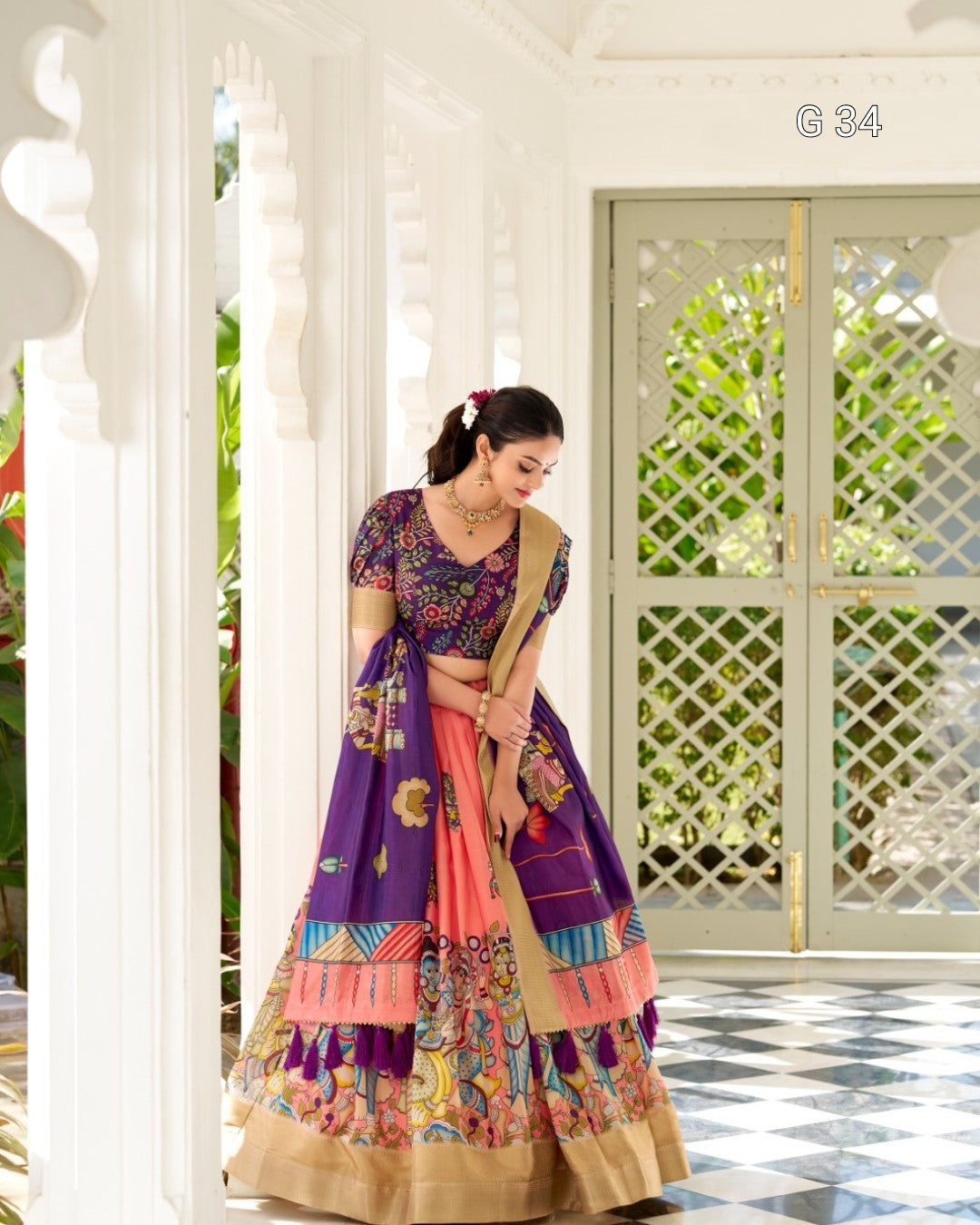 Woman in a colorful traditional outfit standing in a decorative interior setting.