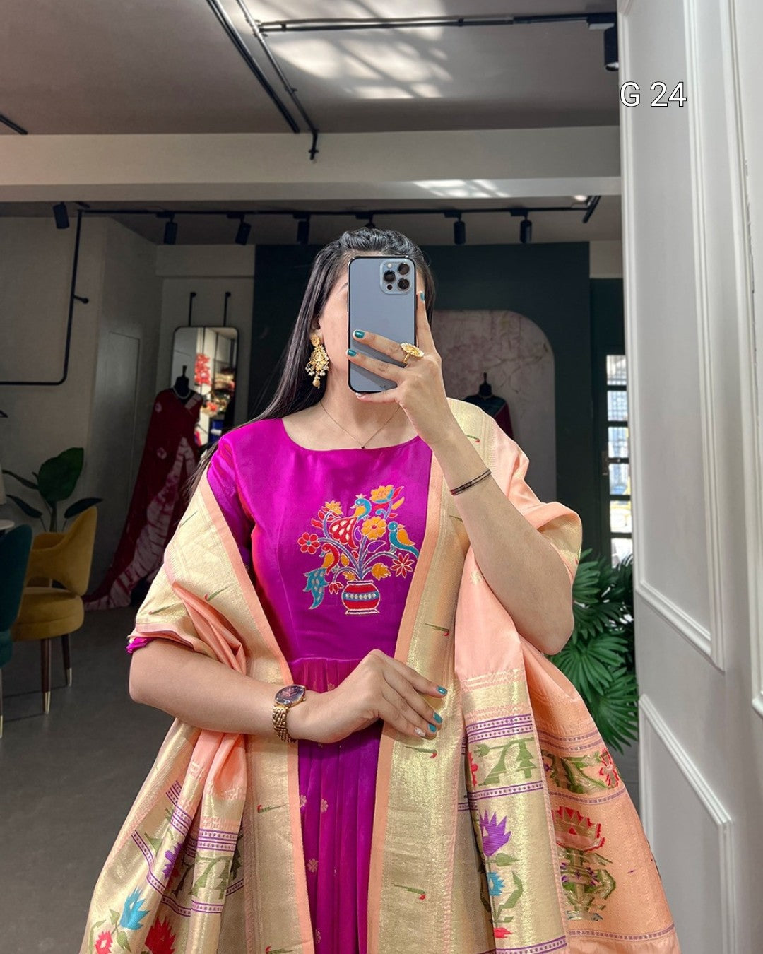 Person wearing a pink dress with floral patterns and an orange dupatta with intricate designs, standing indoors.