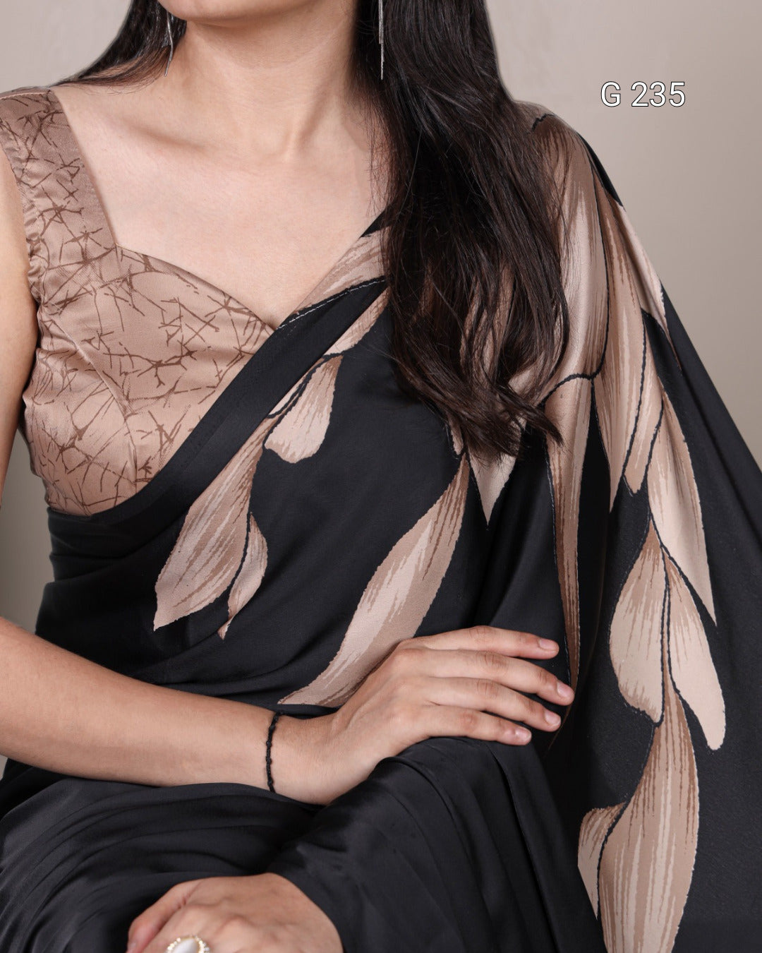 Woman wearing a black saree with a floral pattern, sitting against a neutral background.