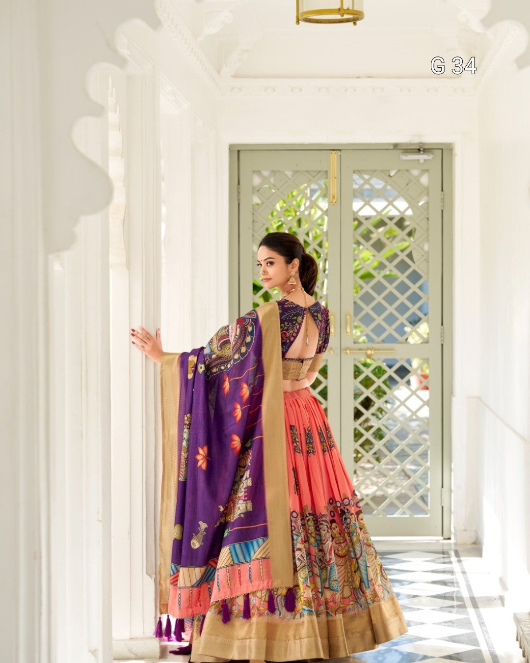 Woman in a colorful traditional outfit standing in a bright room with white walls and a decorative door.