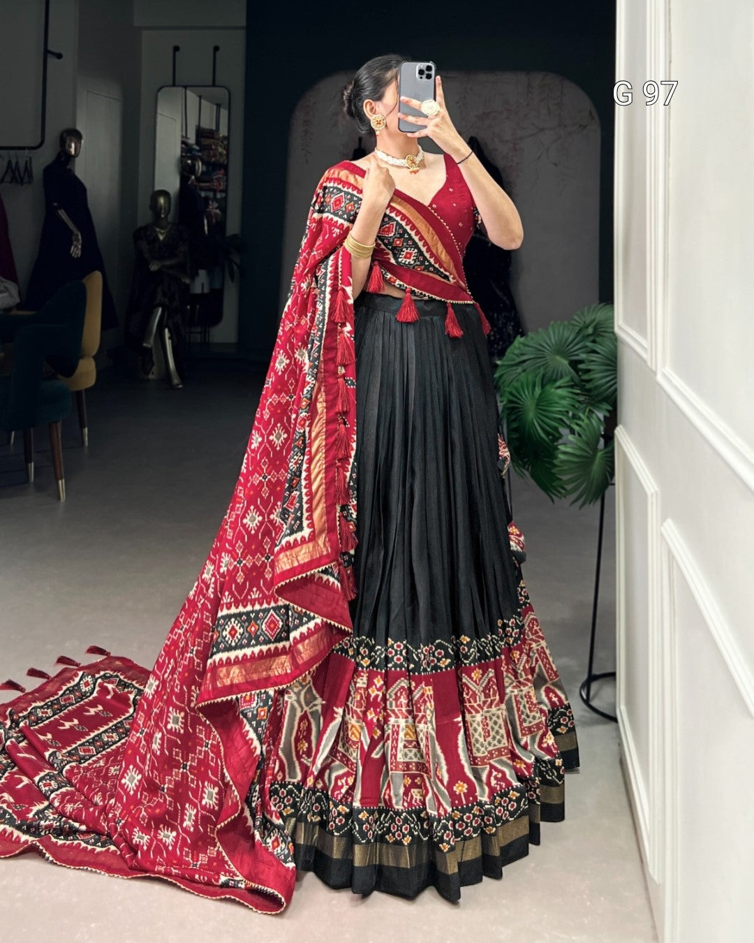 Woman in a traditional outfit with a red and black patterned shawl in a room.