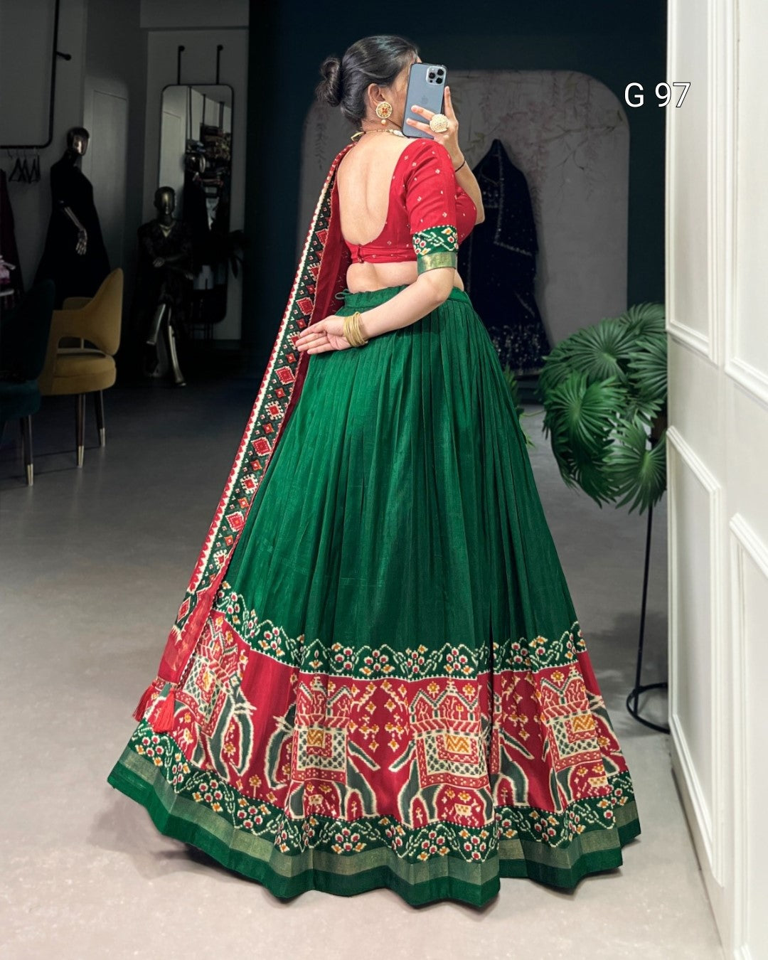 Woman wearing a traditional green and red lehenga with elephant patterns, standing in a room.