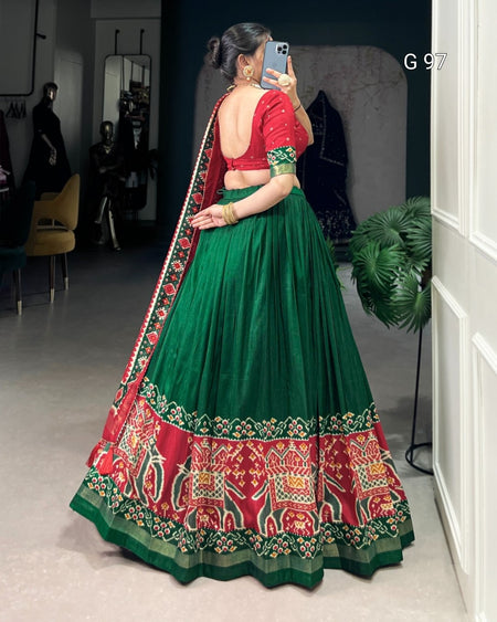 Woman wearing a traditional green and red lehenga with elephant patterns, standing in a room.