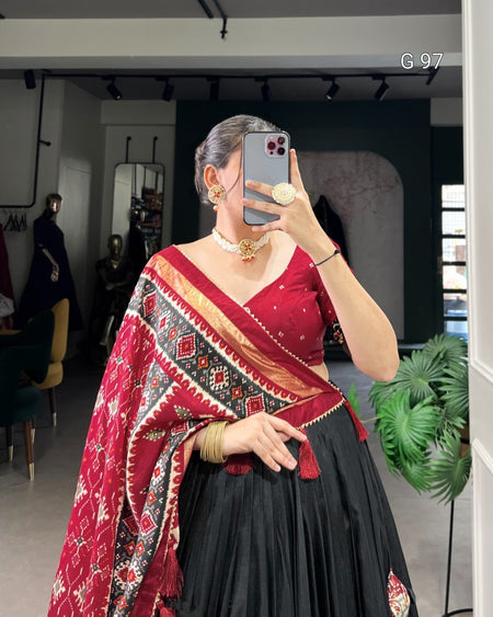 Person wearing a red and black traditional outfit with a patterned shawl, taking a mirror selfie.