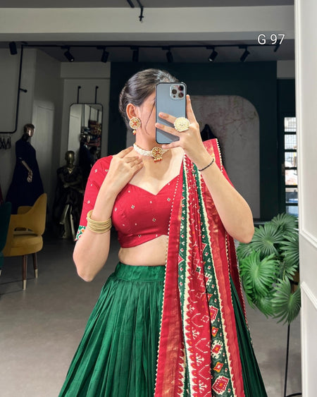 Person wearing a red and green traditional outfit with a patterned dupatta, taking a mirror selfie.