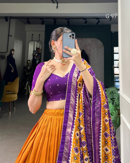 Person wearing a purple and orange traditional outfit with a patterned scarf, taking a mirror selfie.