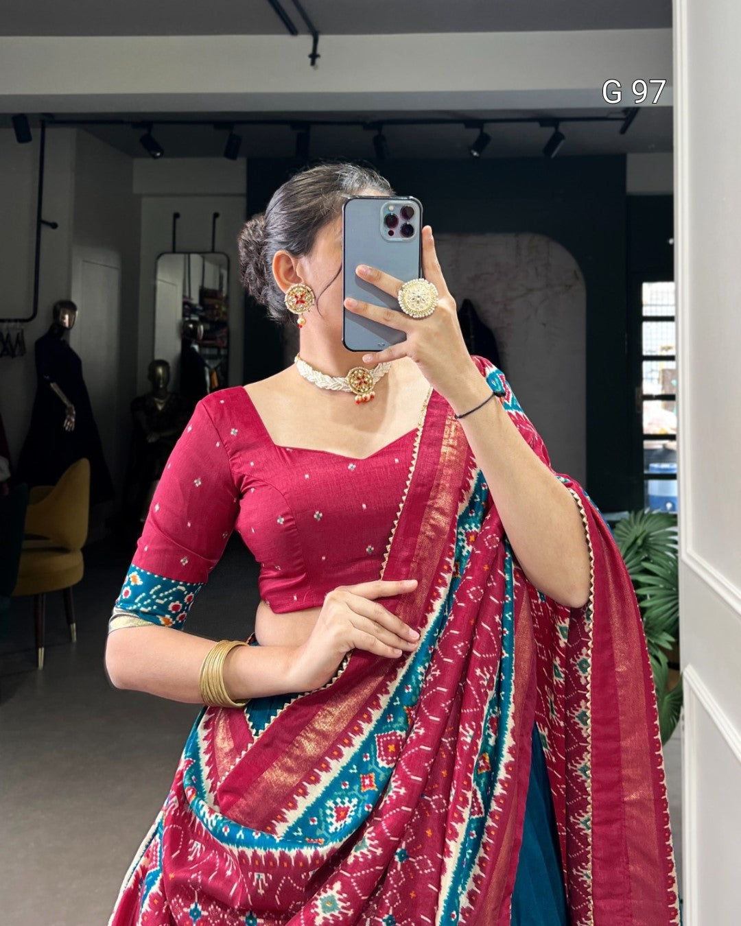 Woman taking a mirror selfie wearing a red saree with blue patterns indoors.