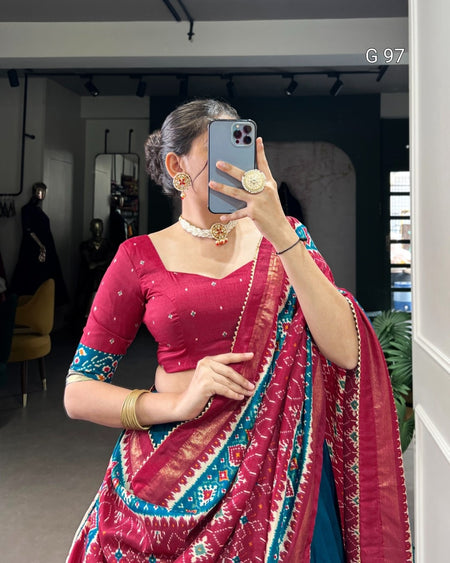 Woman taking a mirror selfie wearing a red saree with blue patterns indoors.