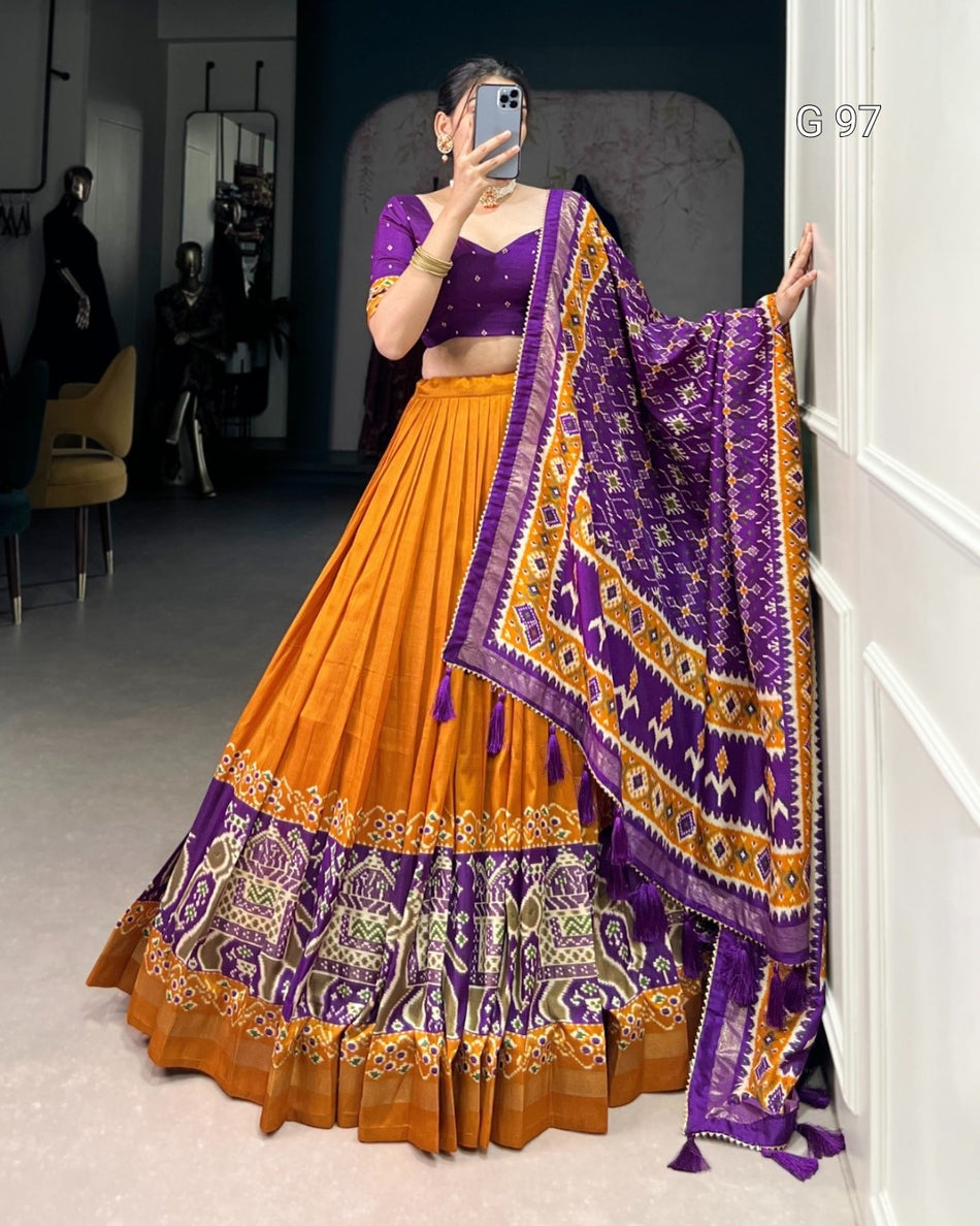 Person wearing a traditional orange and purple outfit with a matching dupatta, standing in a room.