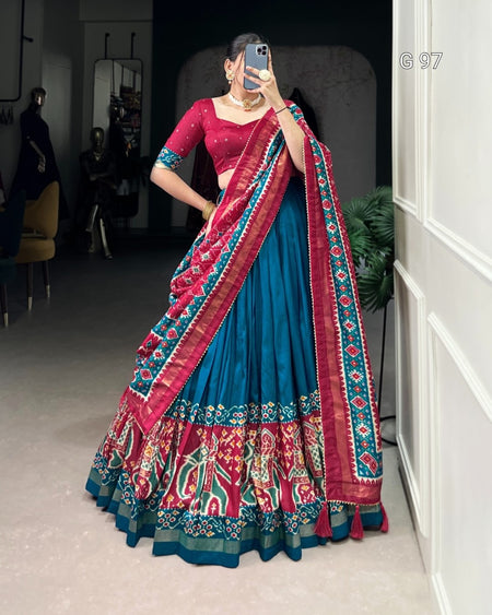 Woman in a traditional blue and red saree with intricate patterns, standing indoors.