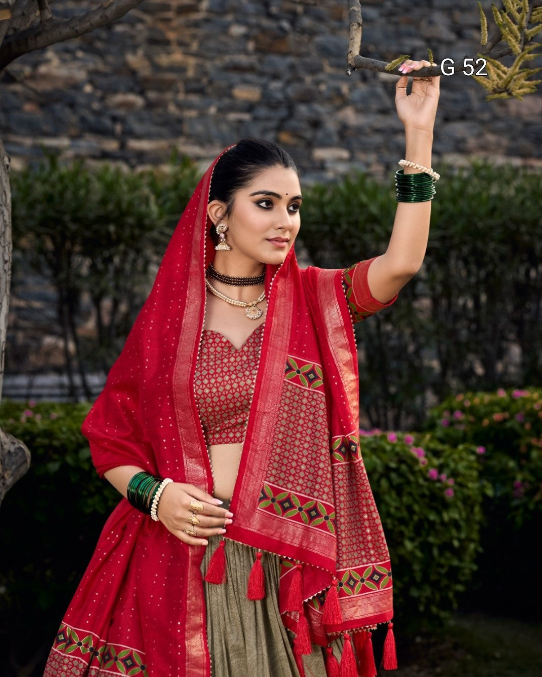 Woman in traditional red and beige outfit with a stone wall and greenery background