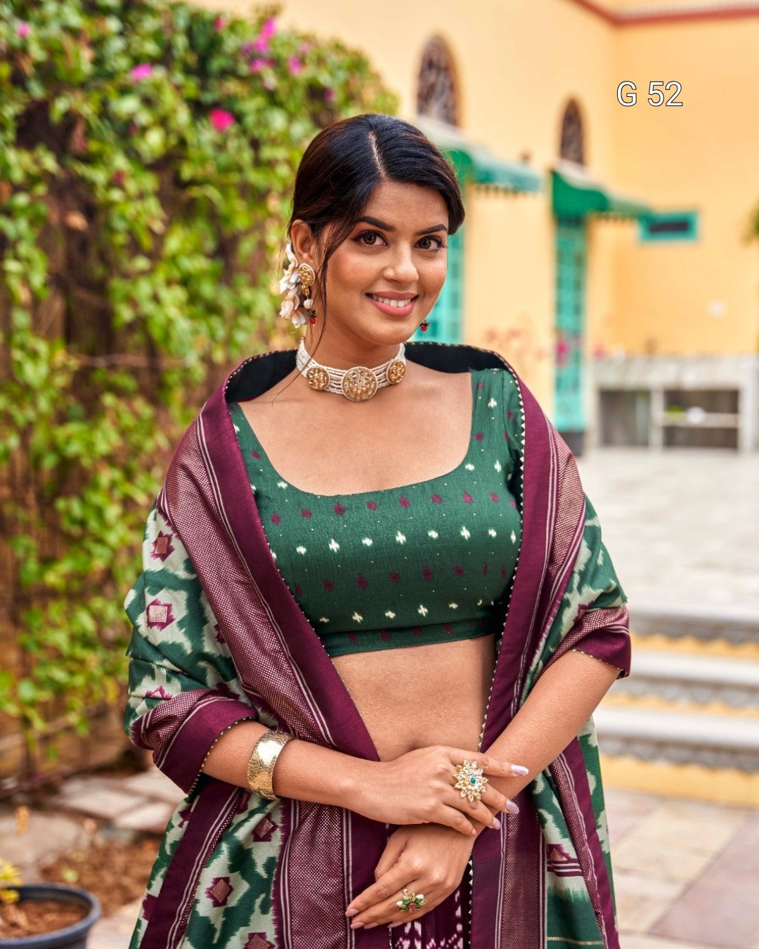 Woman in traditional attire with a green blouse and maroon saree standing outdoors.