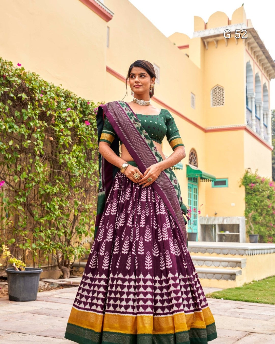 Woman in a traditional outfit with a patterned skirt and purple blouse standing outdoors.